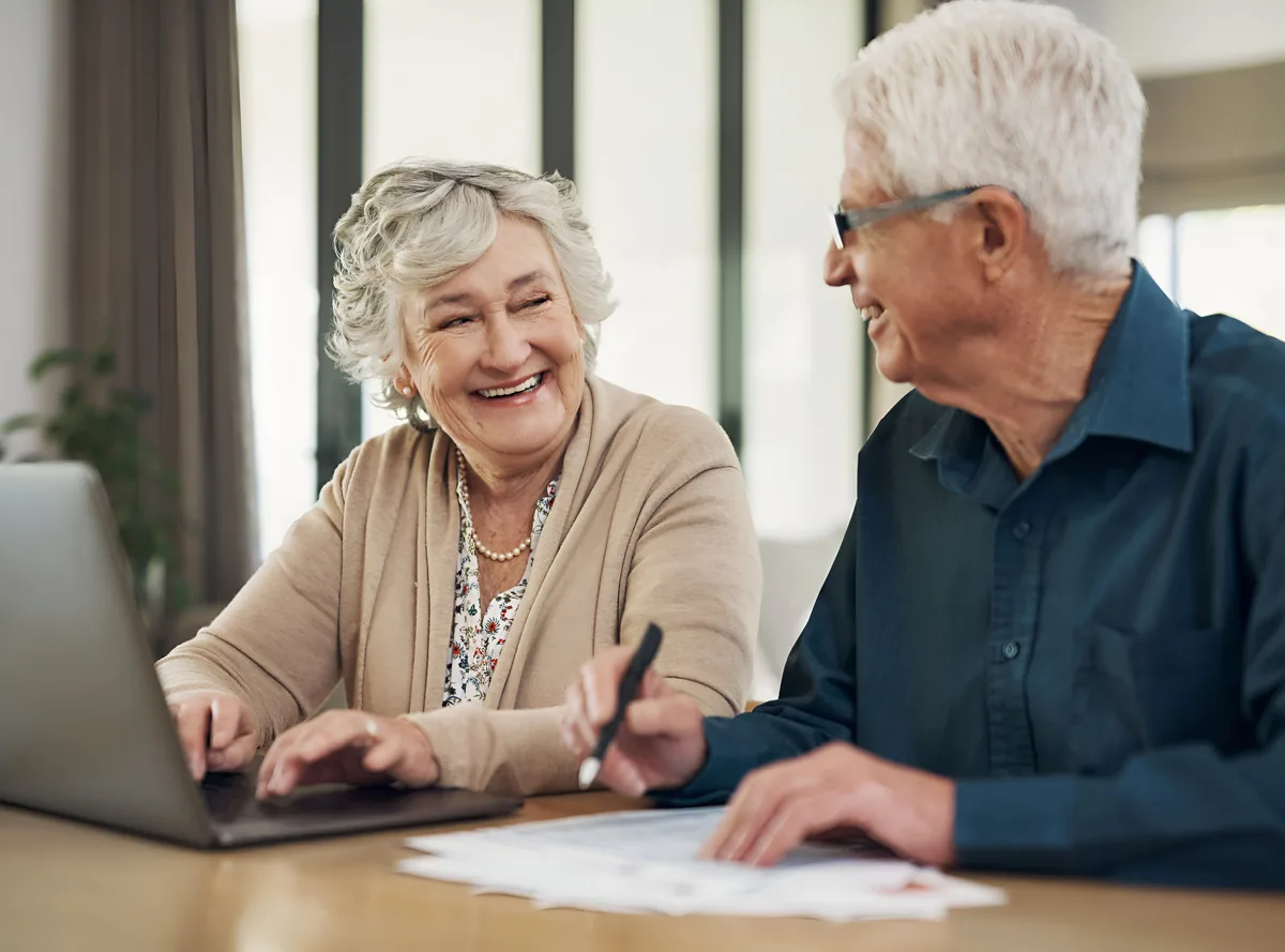 A smiling senior couple completing forms together on a laptop